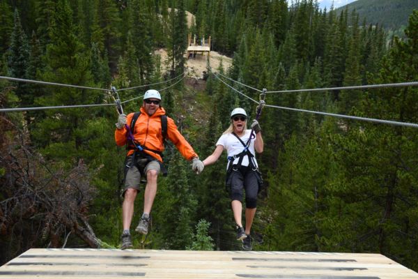 two people side by side on a zip line ride with top of the rockies