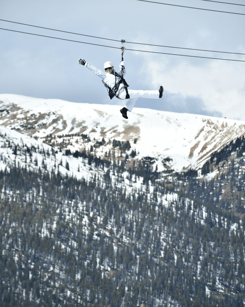 person above the trees waving from the best zipline in Colorado