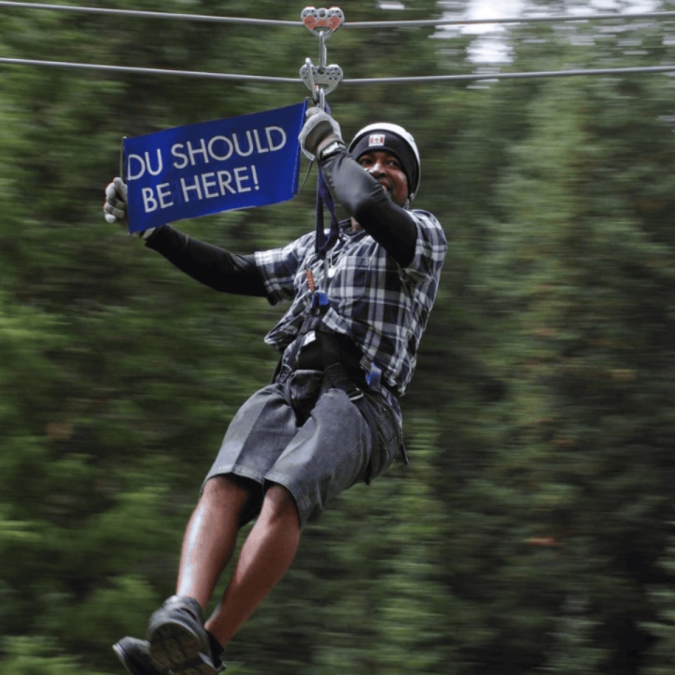 person holding a sign that says You Should Be Here while on a zip line in Colorado