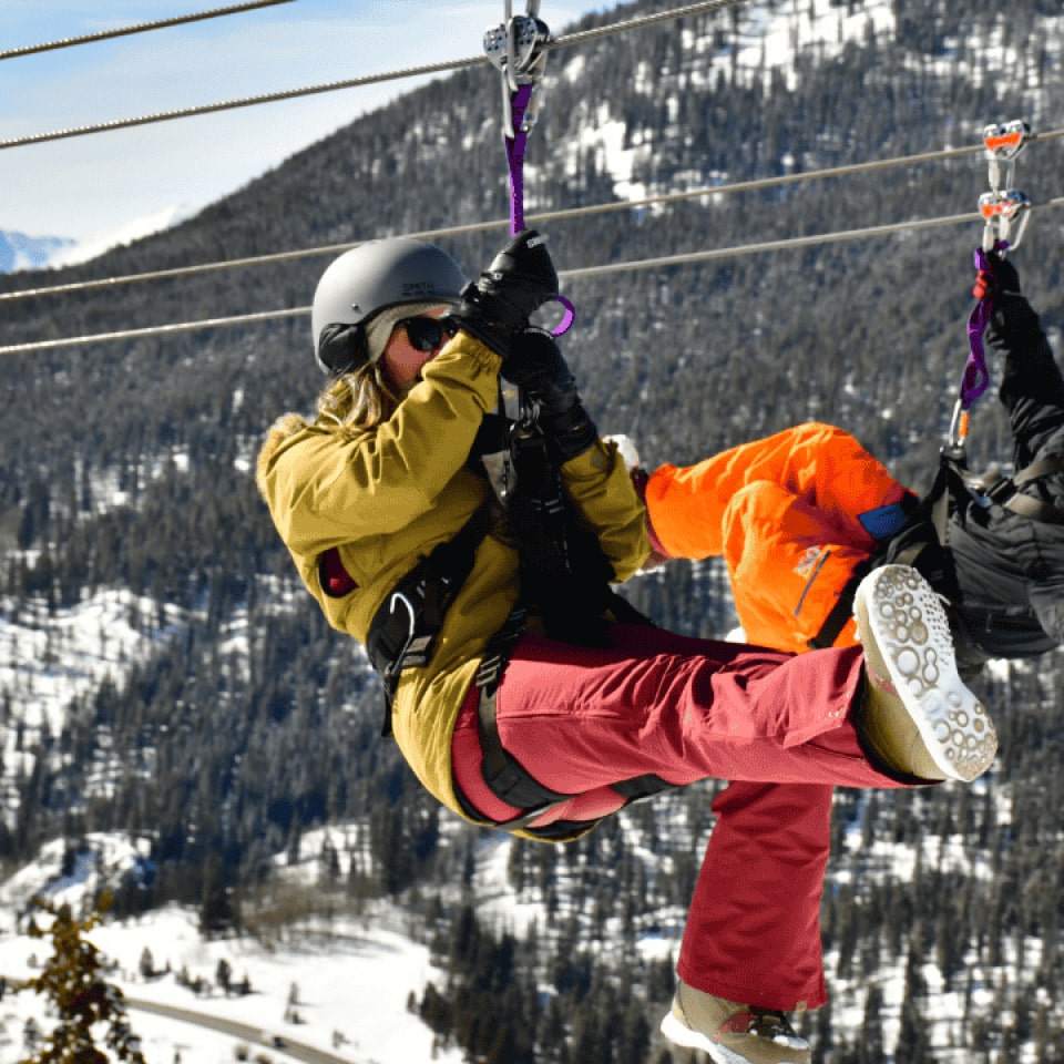 people zip lining in Colorado with mountains and trees in the background