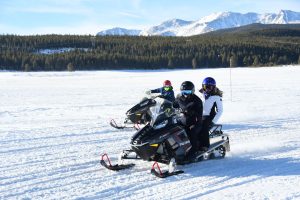 people snowmobiling with trees and mountains in the background