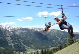 two people on a zipline with mountains and trees behind
